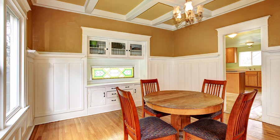 White and mustard dining room with a coffered ceiling and hardwood floor. Built-in antique white cabinet